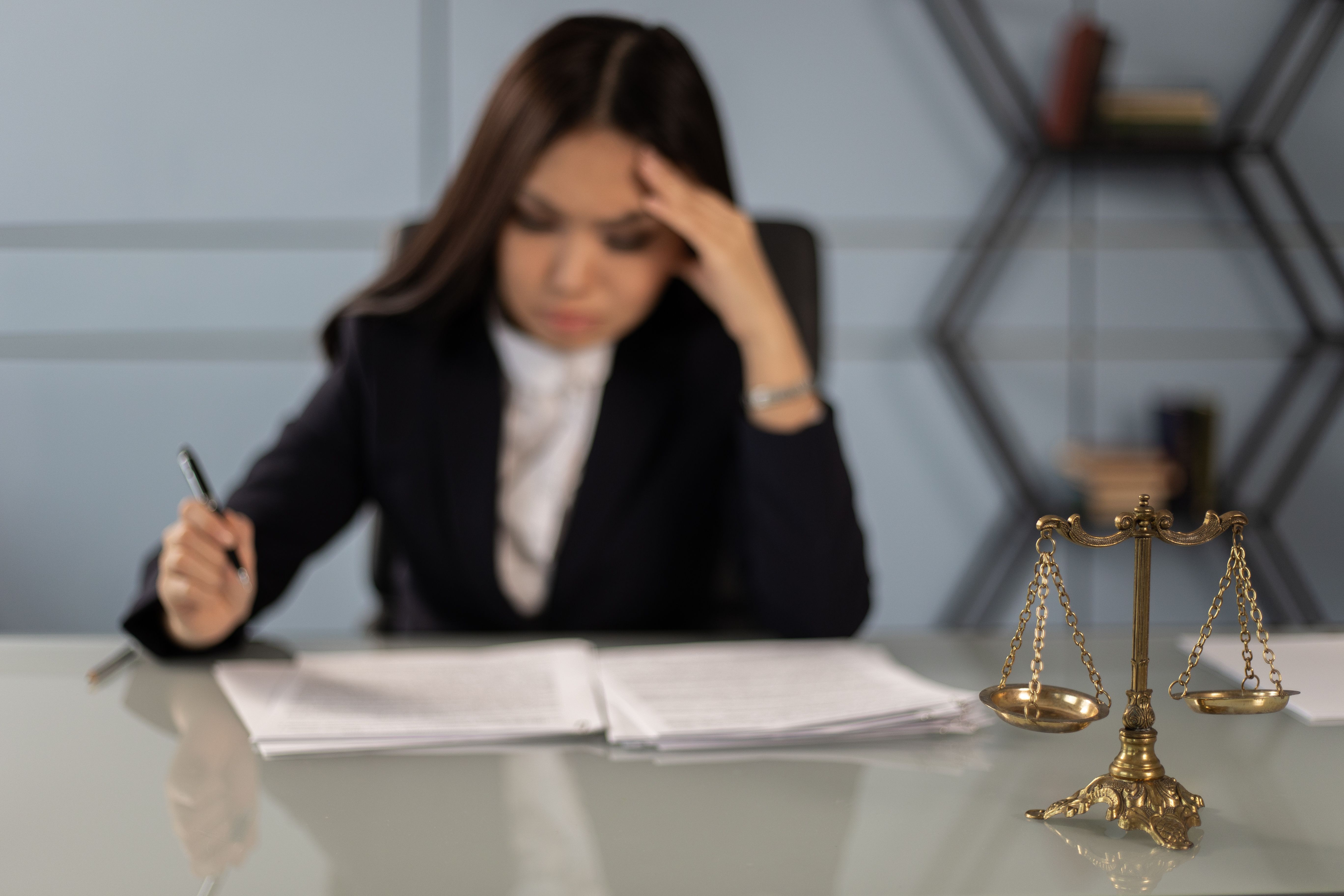 Fatigued lawyer reviewing documents beside a justice scale, illustrating financial stress at a law firm