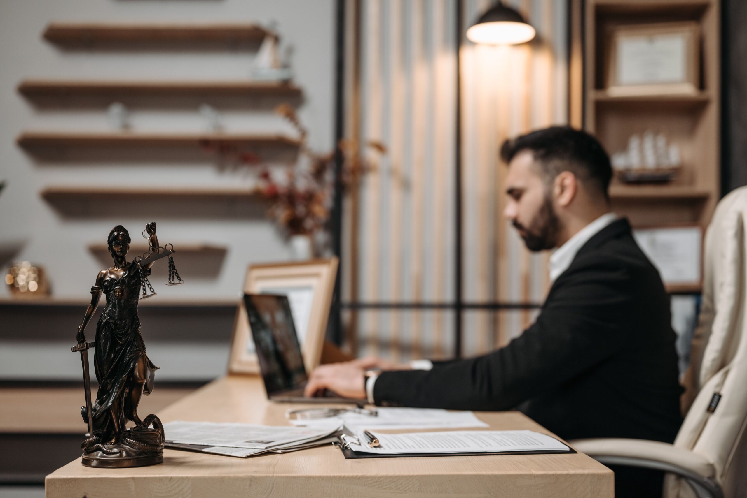 Lawyer working on a laptop in a modern law office with a Lady Justice statue on the desk
